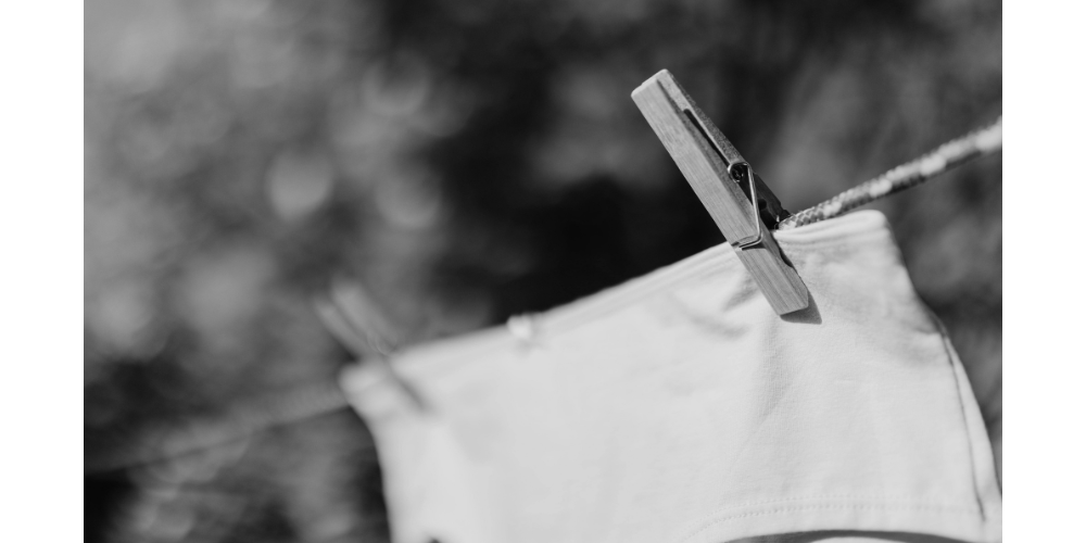 Culotte d'incontinence séchant à l'air libre sur un étendoir, en noir et blanc, végétation en fond.