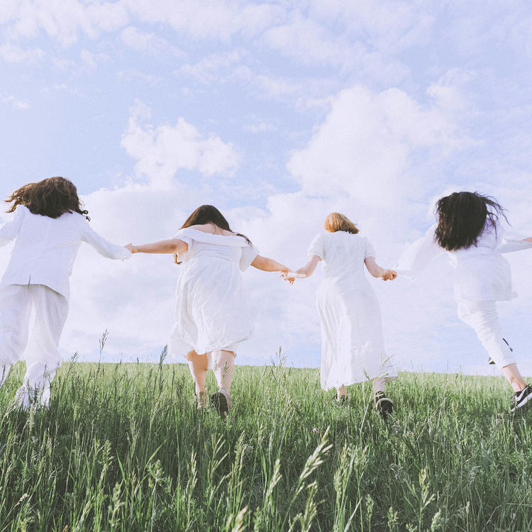 4 femmes habillées en blanc se tiennent la main et marchent ensemble vers l'avant dans la nature.